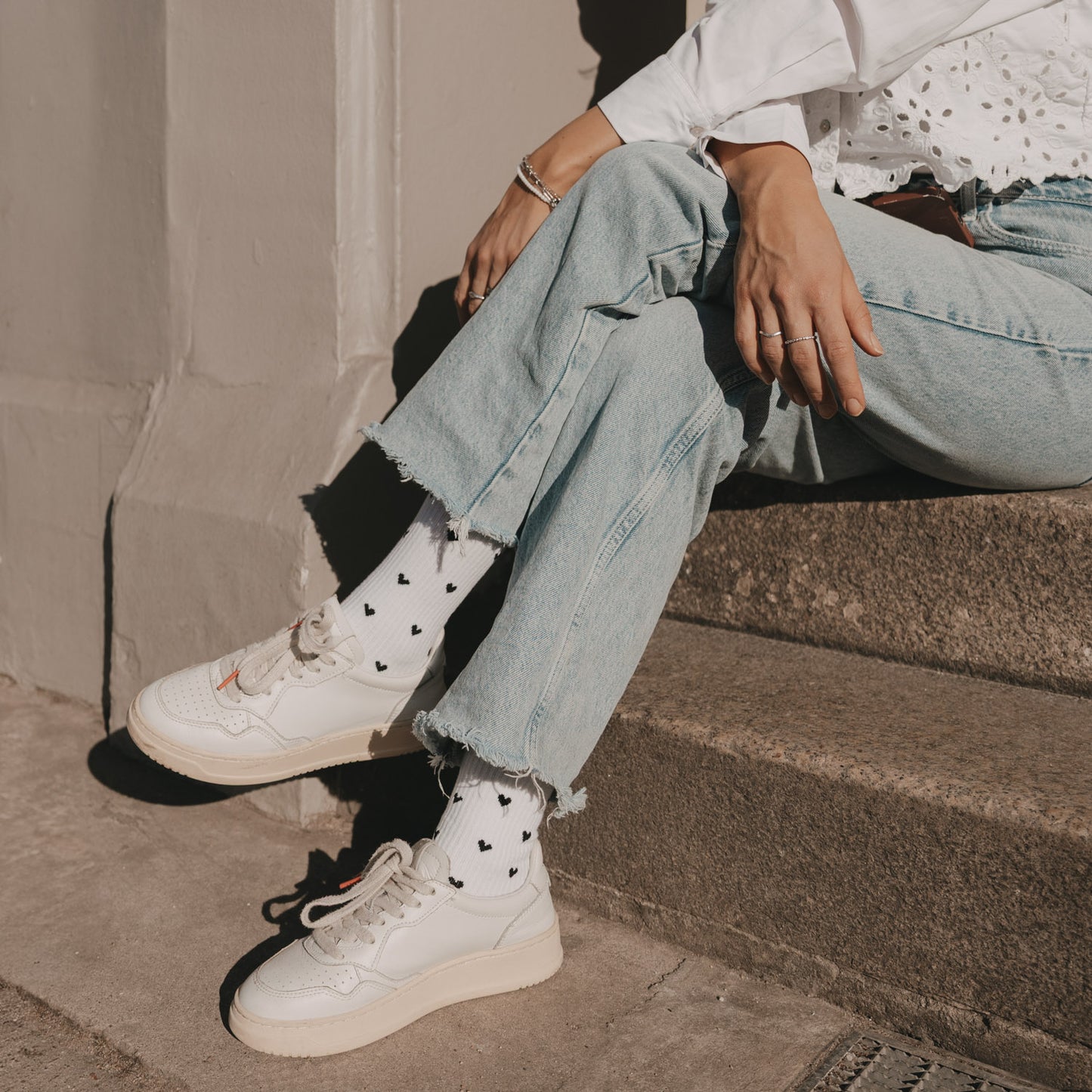 Weiße Herz-Socken in lässigem Outfit beim Sitzen auf Treppe mit Jeans und Sneakern