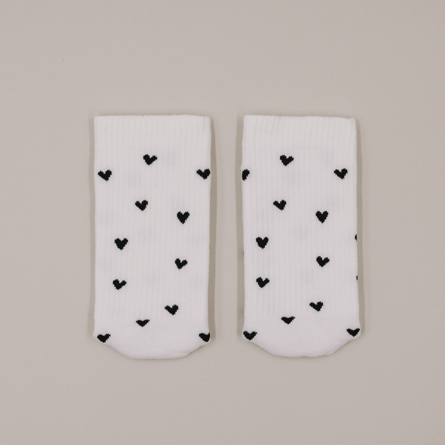 Flachliegende weiße Socken mit schwarzem Herzmuster minimalistisch präsentiert