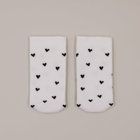 Flachliegende weiße Socken mit schwarzem Herzmuster minimalistisch präsentiert