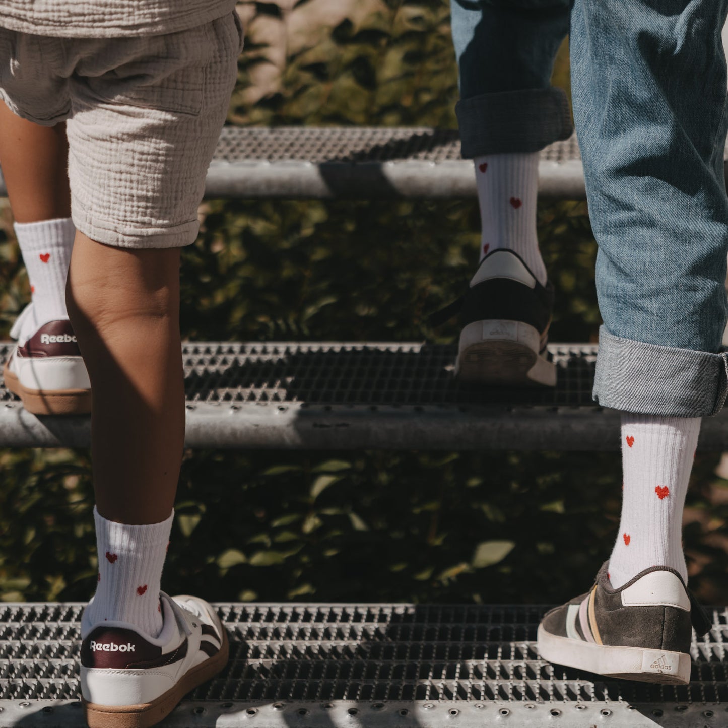 Zwei Kinder tragen Eulenschnitt Kindersocken mit roten Herzen beim gemeinsamen Treppensteigen.