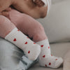 Babybeine mit weißen Herzsocken in Händen gehalten, liebevolle Szene mit weichen Textilien