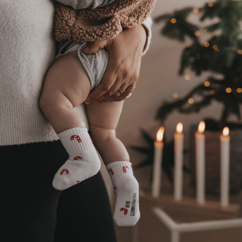 Baby auf dem Arm mit weißen Socken und Zuckerstangen Muster, weihnachtliche Stimmung mit Kerzen