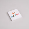 Streichholzschachtel mit bunter Aufschrift BE HAPPY auf weißem Karton, moderne Geschenkidee.
