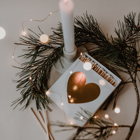 Geöffnete Schachtel mit goldenem Herz, Streichhölzern und Weihnachtsdeko – gemütliches Kerzenlicht-Ambiente.
