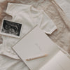 Schwangerschaftstagebuch offen mit Seite „Dein Name“ neben Babybody und Ultraschallfoto.