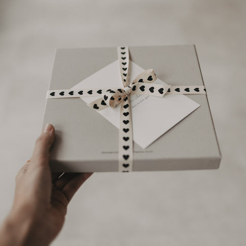 Graue Geschenkbox mit Schleife aus Geschenkband mit schwarzen Herzen.