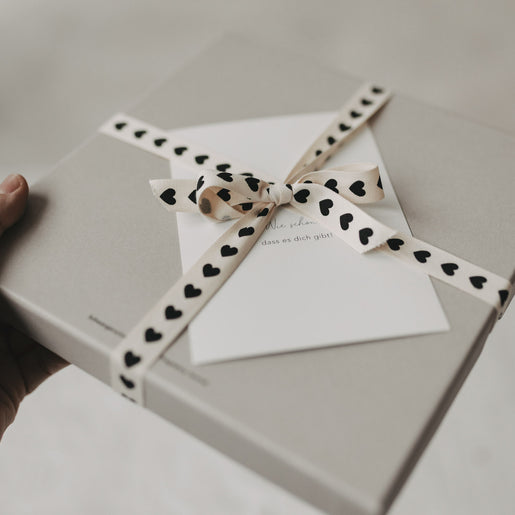 Graue Geschenkbox mit Schleife aus Geschenkband mit schwarzen Herzen.