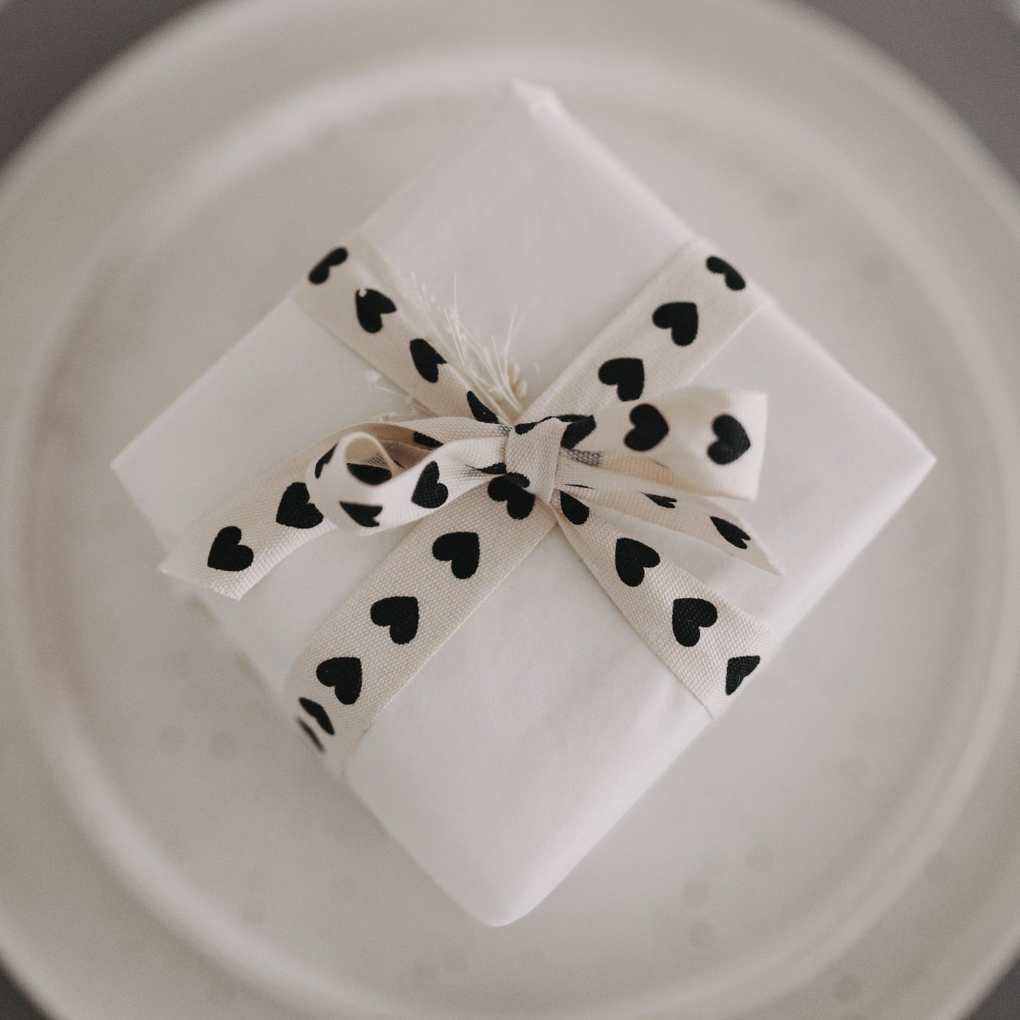 Kleines Geschenk mit Geschenkband mit schwarzen Herzen auf Teller.
