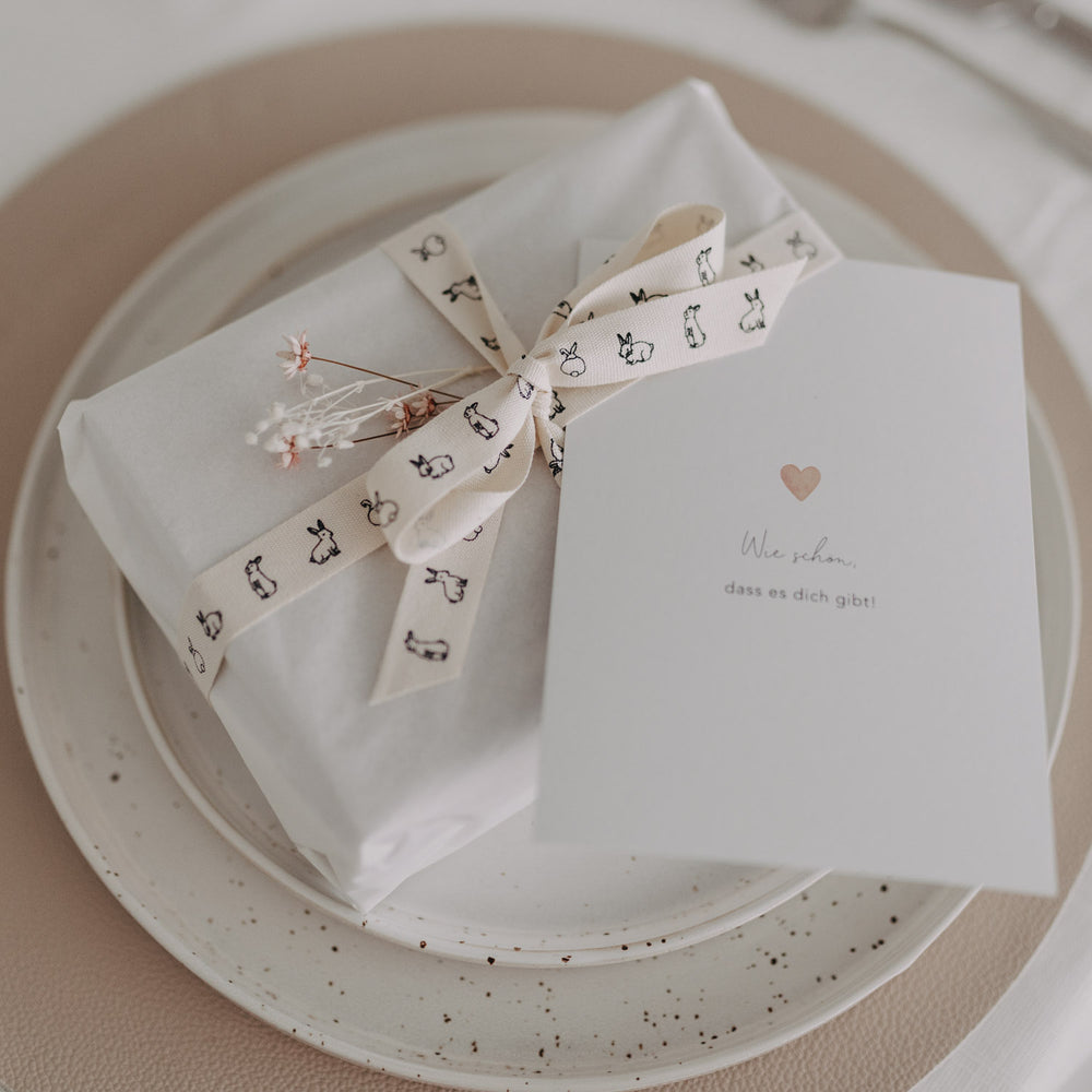 Geschenk mit weißem Papier und Kaninchen-Geschenkband, dekoriert mit Karte und Trockenblumen.