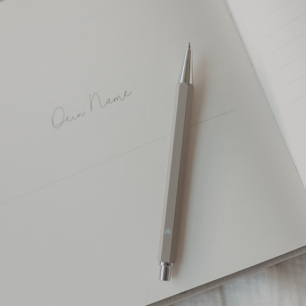 Grauer Druckbleistift auf offener Notizbuchseite mit Schriftzug ‚Dein Name‘.