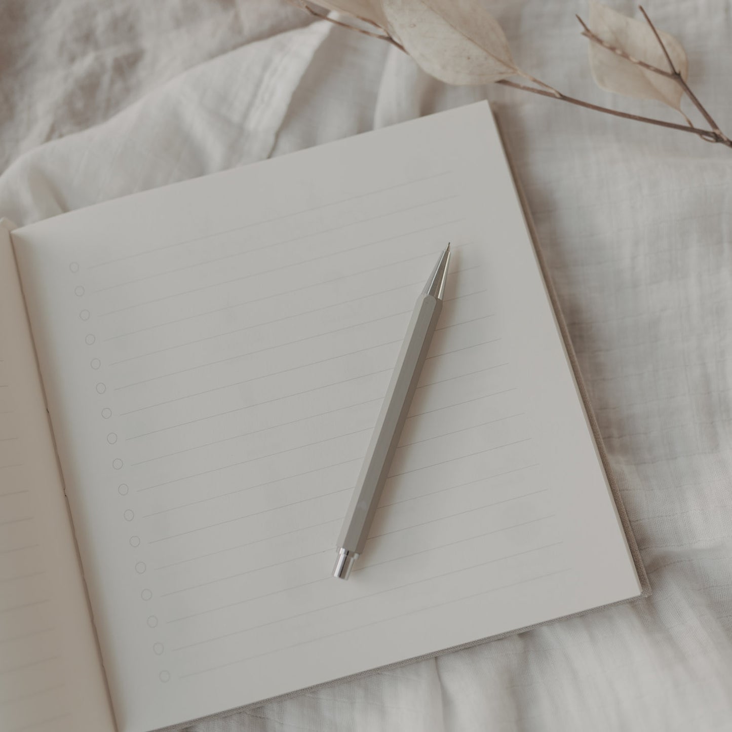 Grauer Druckbleistift auf linierten Notizbuchseiten, stilvoll präsentiert auf weißem Stoff.