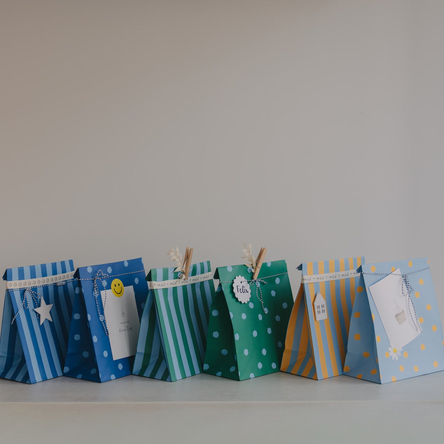 Geschenktüten aus Papier in Blau, Grün und Gelb mit Punkten und Streifen, dekorativ aufgereiht