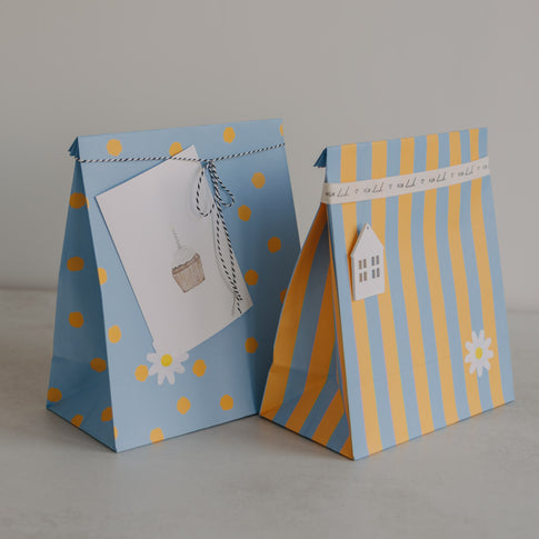 Zwei Papier-Geschenktüten in Hellblau und Gelb mit Punkten und Streifen, liebevoll dekoriert