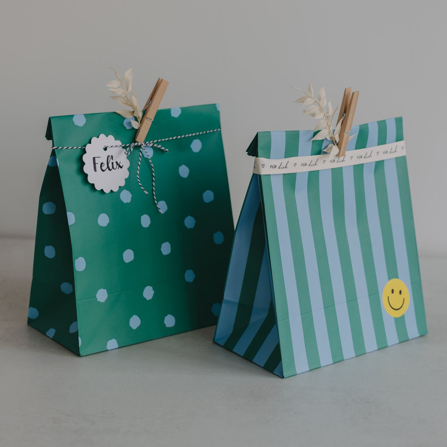 Zwei grüne Papier-Geschenktüten mit Punkten und Streifen, mit Holzklammern verziert