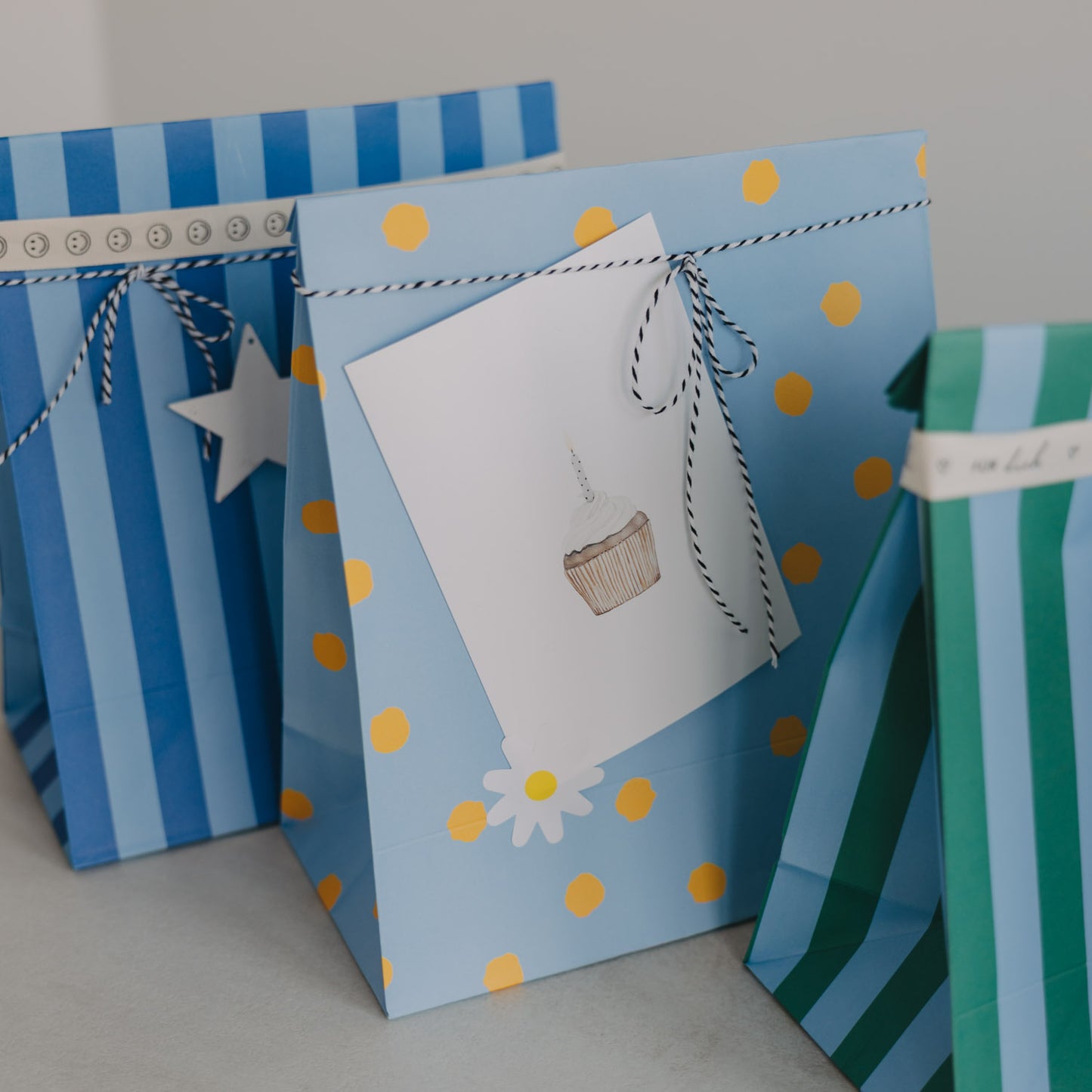 Hellblaue Papier-Geschenktüte mit gelben Punkten und Geschenkanhänger mit Cupcake