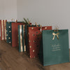 Weihnachtliche Papiergeschenktüten in Grün und Rostrot mit Golddetails, stehend arrangiert auf Holzoberfläche