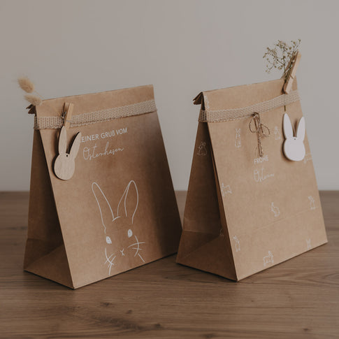 Braune Oster-Geschenktüten aus Papier mit Hasenillustration, Stoffband und Holzanhänger, dekorativ arrangiert