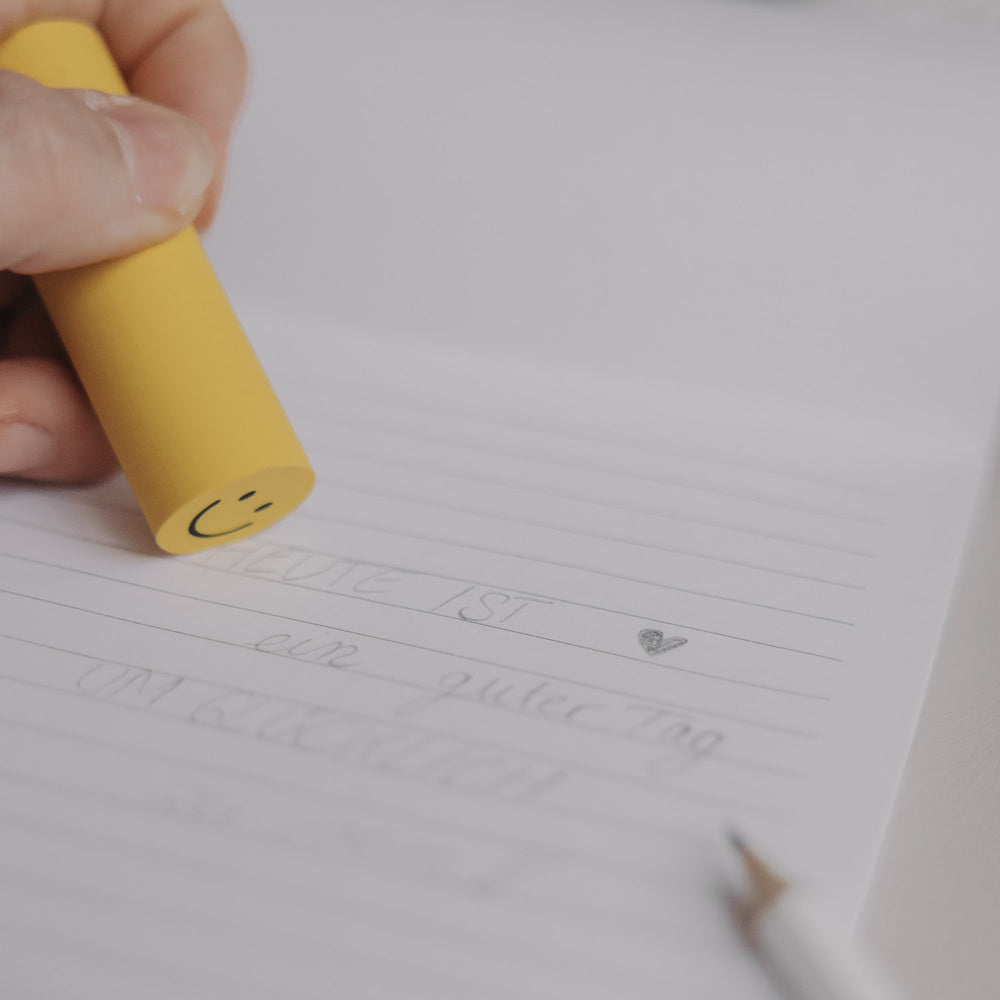 Hand radiert mit gelbem Radiergummi Smiley auf Notizpapier