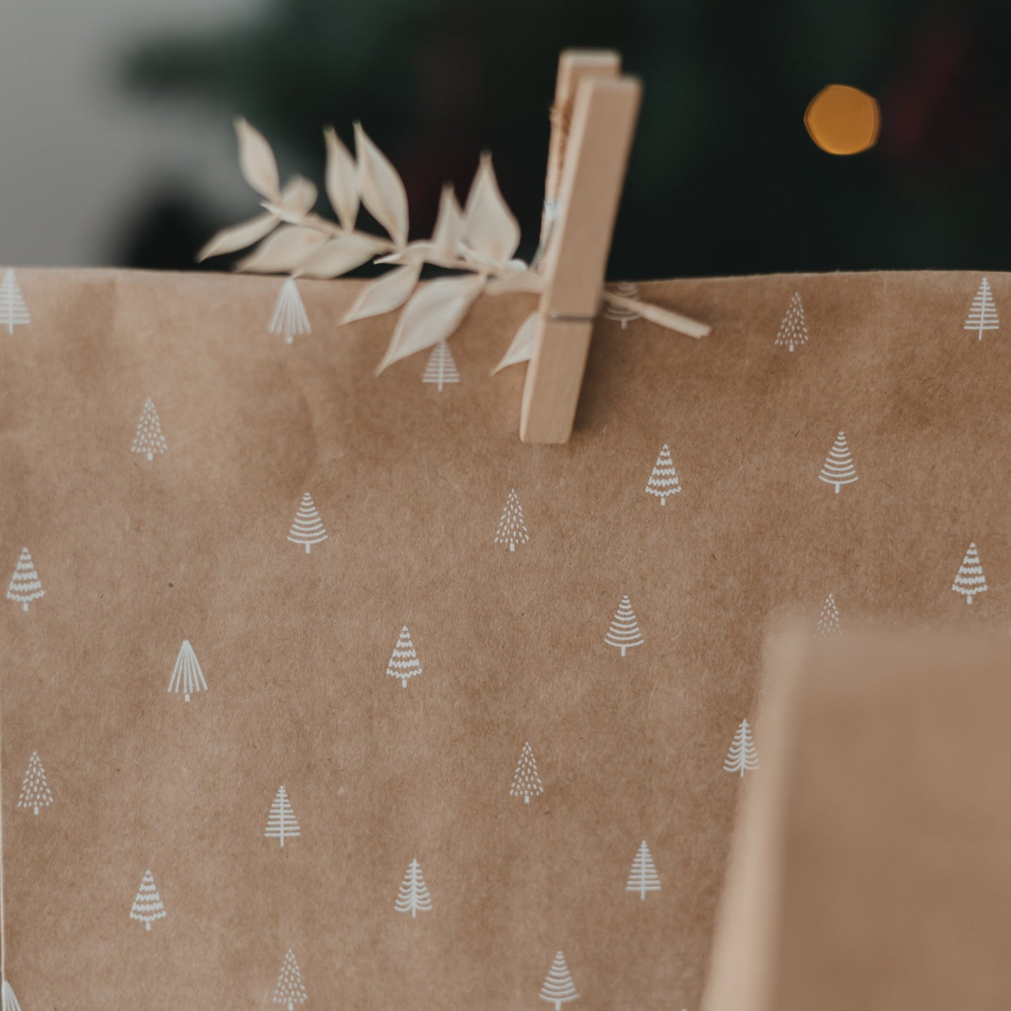 Braune Geschenktüte mit weißen Weihnachtsbaum-Motiven, Holzklammer und dekorativem Zweig