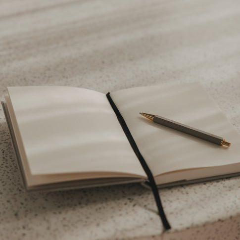 Offenes kariertes A5 Notizbuch mit schwarzem Leseband und Stift auf hellem Untergrund