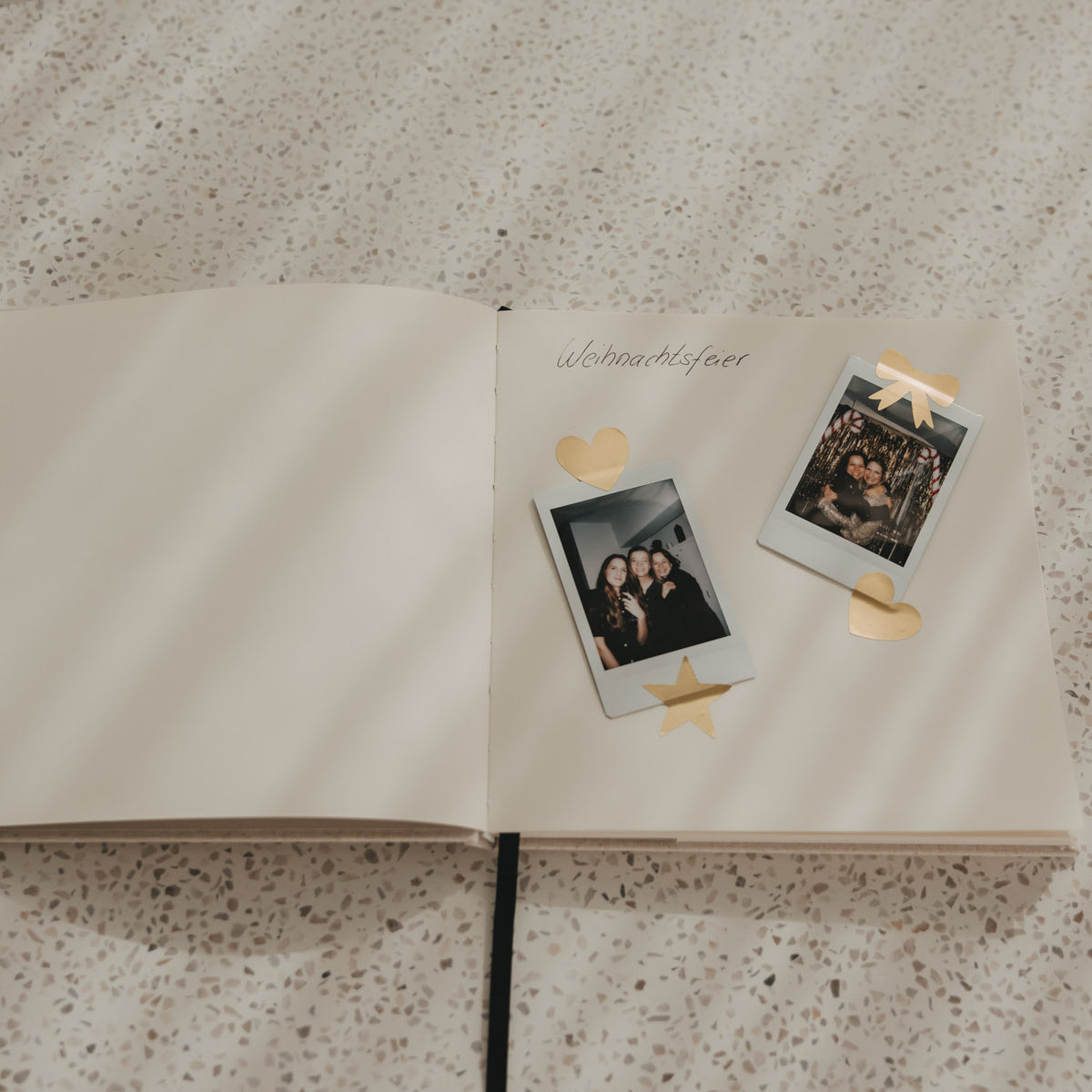 Offenes Buch mit Blankoseiten, eingeklebten Fotos und goldenen Herz-, Stern- und Schleifenstickern