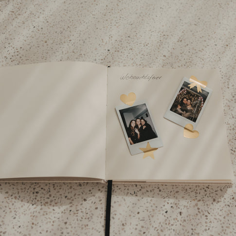 Offenes Buch mit Blankoseiten, eingeklebten Fotos und goldenen Herz-, Stern- und Schleifenstickern
