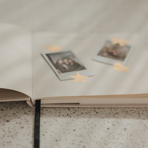 Detailansicht eines offenen Buchs mit Blankoseiten, Fotos und goldenen Stickern